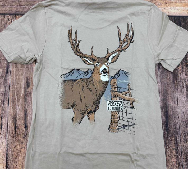 A gray shirt lying flat on a wooden table. The shirt features an image of a deer next to a "No Hunting" sign.