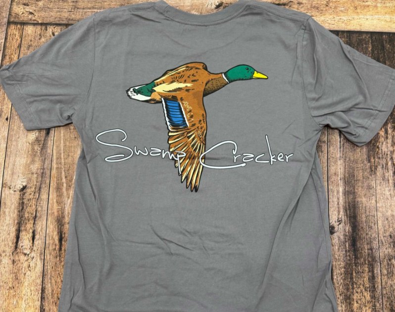 A gray shirt with an image of a duck visible across the front. Text under the text reads "Swamp Cracker."
