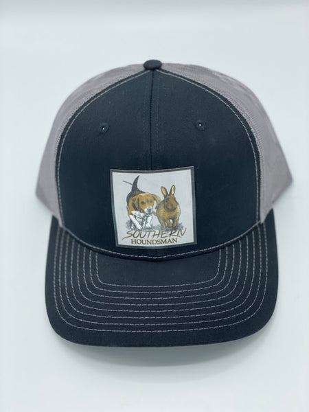 Black and charcoal Southern Houndsman outdoorsman hat from Swamp Cracker Outdoor Apparel with a beagle chasing a rabbit patched on the front.